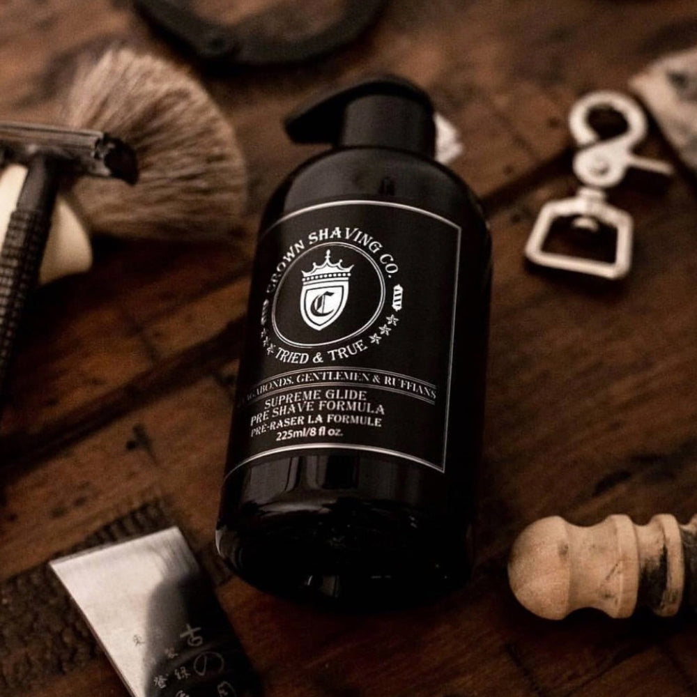 Gros plan d’un flacon d’huile de pré-rasage haut de gamme posé sur une surface en bois, entouré d’accessoires de rasage classiques comme un rasoir, un blaireau et des outils de grooming.