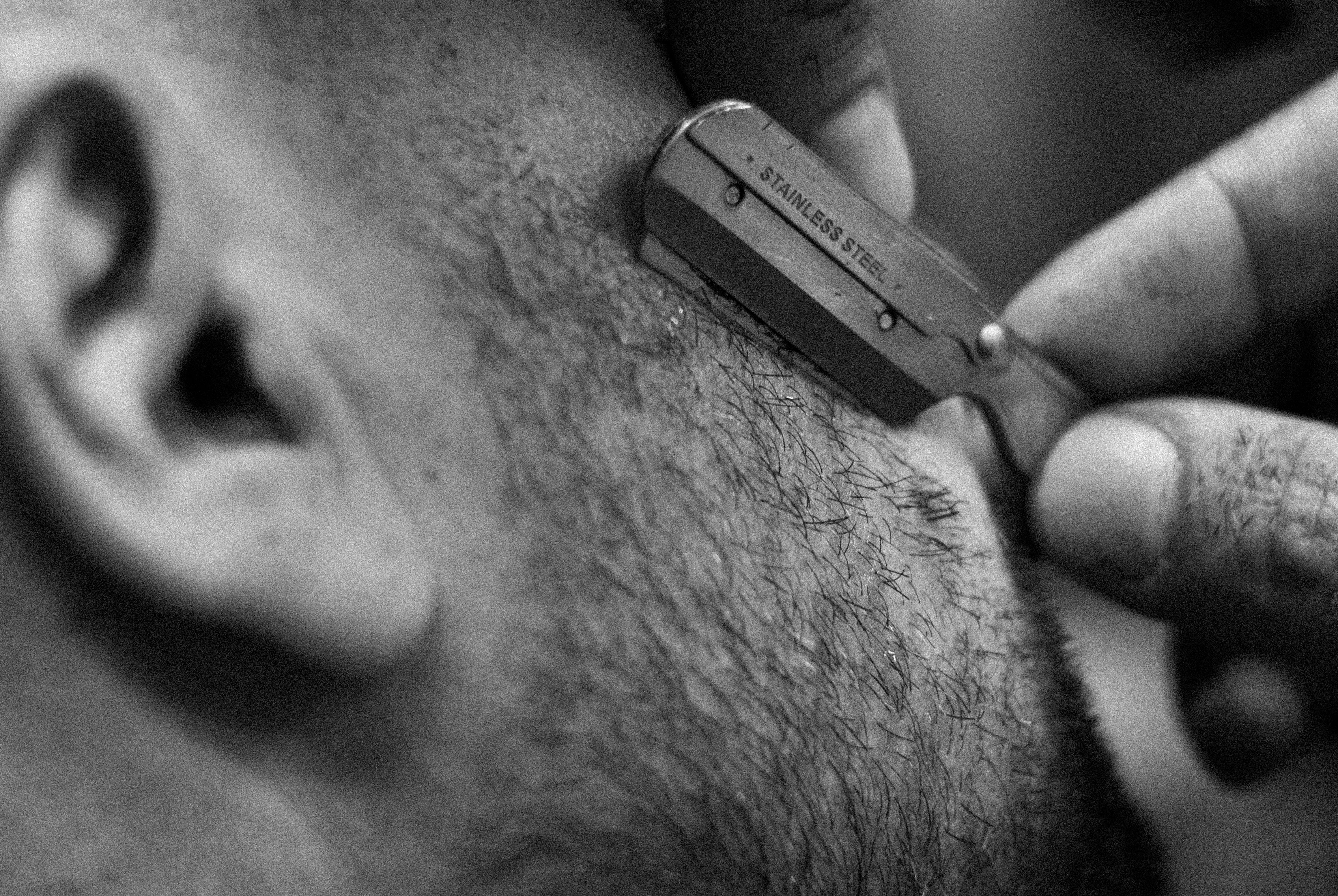 Gros plan en noir et blanc d’un rasoir droit en train de raser une barbe courte